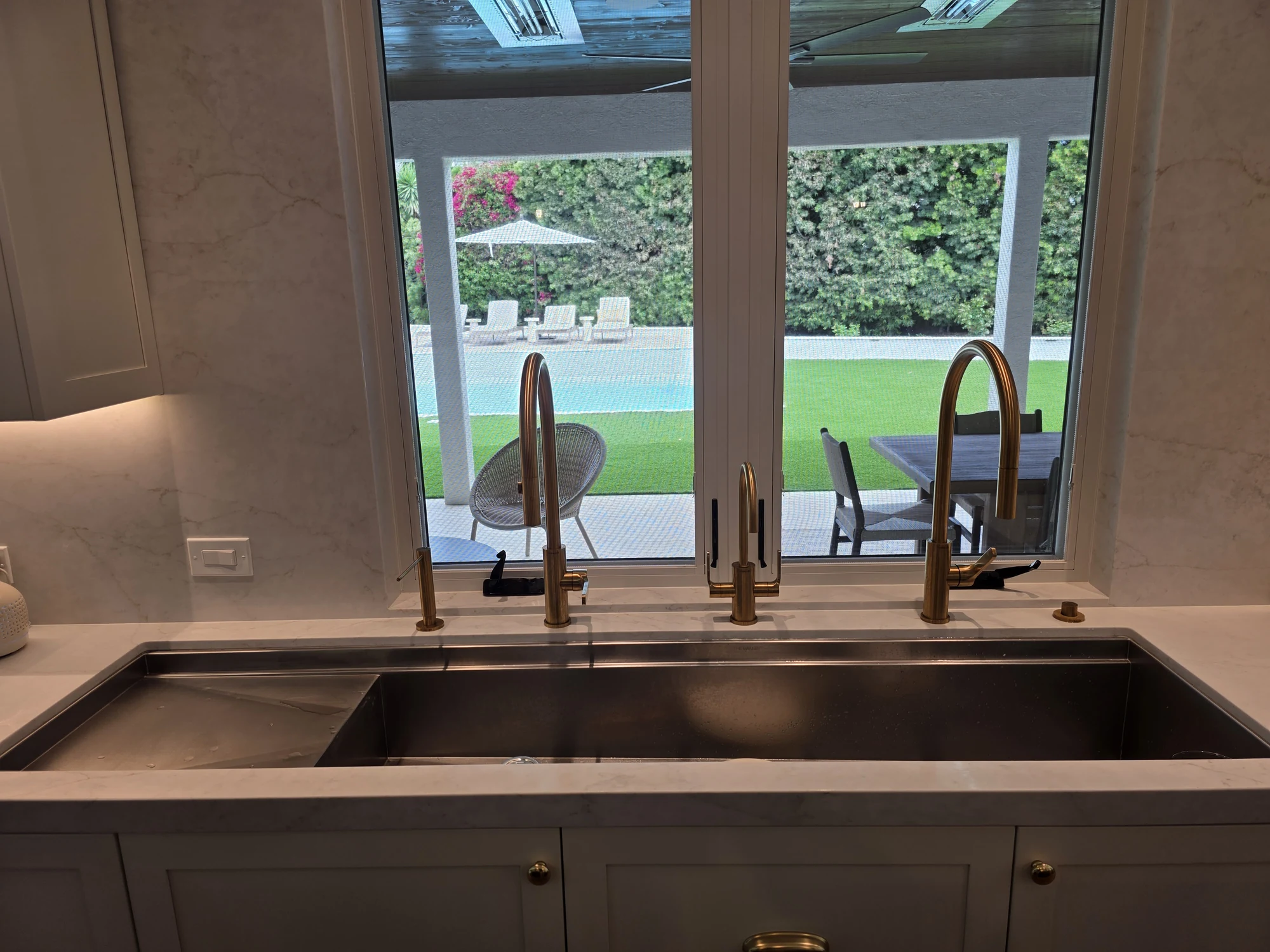 Kitchen sink and brass fittings beneath garden-facing windows